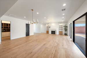 Unfurnished living room featuring a chandelier, a fireplace, light wood-style flooring, and built in shelves