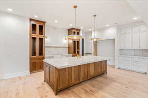 Kitchen featuring brown cabinetry, tasteful backsplash, light wood-type flooring, recessed lighting, and a kitchen island with sink