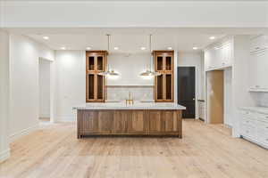 Kitchen with backsplash, pendant lighting, a center island with sink, recessed lighting, and brown cabinetry