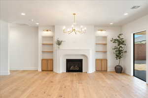 Living room featuring built in shelves, a chandelier, light wood-style flooring, and a glass covered fireplace