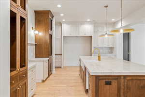 Kitchen with brown cabinets, a center island with sink, recessed lighting, light wood finished floors, and light stone countertops