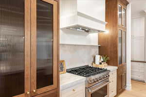Two tone kitchen featuring gas range, glass fronted cabinets, backsplash, dual tone cabinets, and light stone countertops