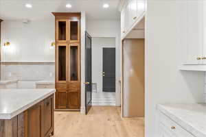 Kitchen with brown cabinetry, recessed lighting, light wood-style floors, white cabinetry, and backsplash