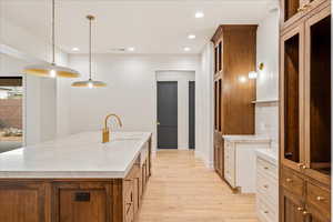 Kitchen featuring pendant lighting, recessed lighting, light wood finished floors, brown cabinetry, and a kitchen island with sink