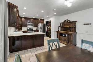 Kitchen featuring dark brown cabinetry, recessed lighting, light tile patterned floors, stainless steel appliances, and a peninsula