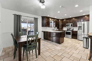 Kitchen with a peninsula, dark brown cabinetry, light countertops, appliances with stainless steel finishes, and backsplash
