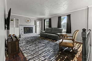 Living room with dark wood finished floors, crown molding, a fireplace, and a textured ceiling