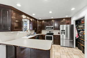 Kitchen with dark brown cabinetry, stainless steel appliances, light countertops, recessed lighting, and a peninsula