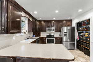 Kitchen featuring dark brown cabinets, light countertops, appliances with stainless steel finishes, backsplash, and recessed lighting