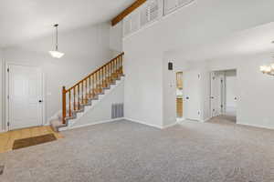 Unfurnished living room with high vaulted ceiling, stairway, light colored carpet, a chandelier, and beamed ceiling