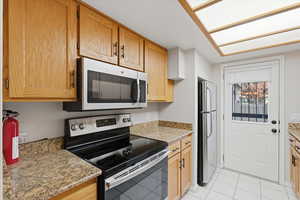 Kitchen featuring appliances with stainless steel finishes, light tile patterned floors, light stone counters, and a skylight