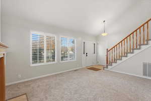 Foyer entrance featuring stairway, light colored carpet, and high vaulted ceiling