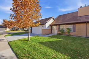 View of front of home featuring a front yard, concrete driveway, brick siding, and a shingled roof