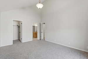 Unfurnished bedroom featuring high vaulted ceiling, a walk in closet, light carpet, and connected bathroom