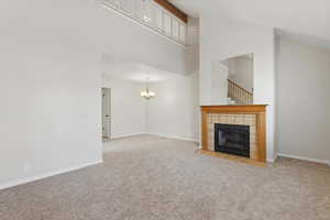 Unfurnished living room with high vaulted ceiling, light colored carpet, a chandelier, and a tile fireplace