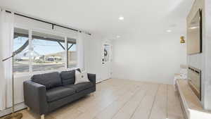 Living room featuring recessed lighting, light wood-type flooring, a glass covered fireplace, a baseboard radiator, and baseboard heating