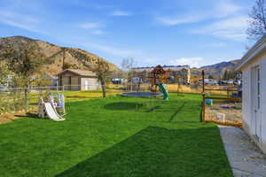 Fenced backyard featuring a playground, a mountain view, and a trampoline