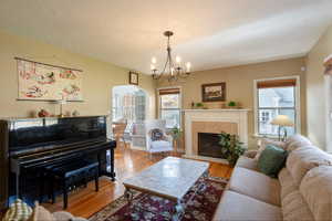 Living room with arched walkways, wood finished floors, a fireplace with flush hearth, a chandelier, and a textured ceiling