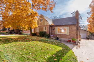 Tudor house with a front lawn, brick siding, a chimney, and roof with shingles