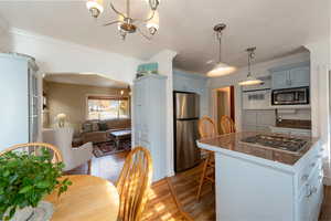 Kitchen with ornamental molding, hanging light fixtures, dark wood-style flooring, appliances with stainless steel finishes, and a chandelier