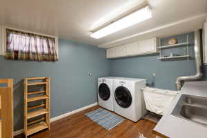 Laundry room with dark wood-style floors, cabinet space, and washing machine and dryer