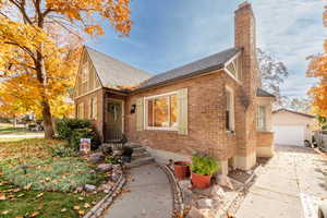 Tudor home featuring brick siding, a chimney, an outbuilding, roof with shingles, and driveway