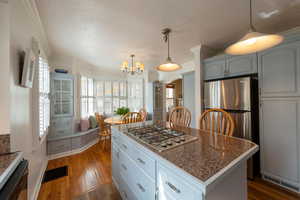 Kitchen with decorative light fixtures, appliances with stainless steel finishes, a center island, a textured ceiling, and dark wood-type flooring