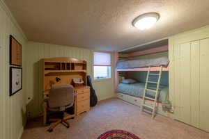 Bedroom featuring light colored carpet, a textured ceiling, and wooden walls