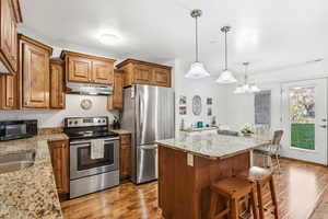 Kitchen featuring brown cabinetry, appliances with stainless steel finishes, a center island, a breakfast bar area, and dark wood-type flooring