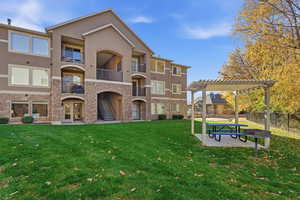 Rear view of property featuring a balcony, stucco siding, a patio area, stone siding, and a yard