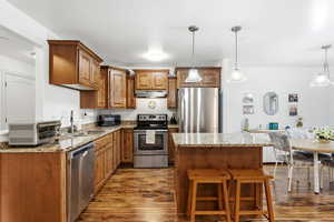 Kitchen with brown cabinets, a center island, light stone counters, stainless steel appliances, and hanging light fixtures