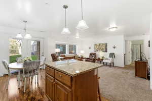 Kitchen with brown cabinetry, light stone countertops, pendant lighting, open floor plan, and a center island