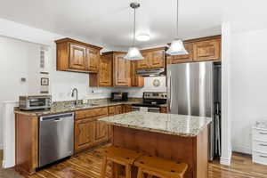 Kitchen featuring brown cabinetry, light stone counters, a kitchen island, and stainless steel appliances