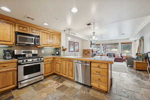 Kitchen featuring decorative backsplash, pendant lighting, a raised ceiling, appliances with stainless steel finishes, and open floor plan