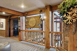 Corridor featuring wooden walls, carpet floors, a textured ceiling, an upstairs landing, and beam ceiling