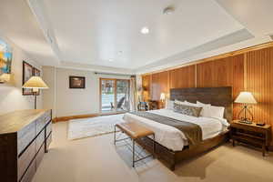 Bedroom with light carpet, wood walls, a tray ceiling, access to exterior, and recessed lighting