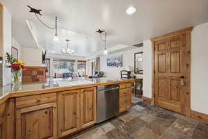 Kitchen with decorative light fixtures, stone tile floors, open floor plan, brown cabinets, and dishwasher