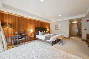 Bedroom with light colored carpet, an office area, and wooden walls