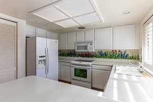 Kitchen featuring white appliances, light countertops, and white cabinets, pantry and pass through window.