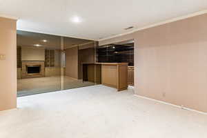 Unfurnished living/den area featuring a textured ceiling, a fireplace, crown molding, carpet, and recessed lighting