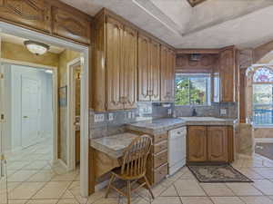 Kitchen featuring brown cabinetry, healthy amount of natural light, light tile patterned floors, and tasteful backsplash