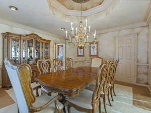 Dining area with a raised ceiling, ornamental molding, a chandelier, and light colored carpet