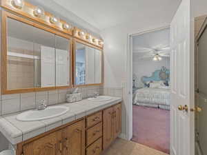 Ensuite bathroom featuring light colored carpet, double vanity, a shower with door, light tile patterned flooring, and backsplash