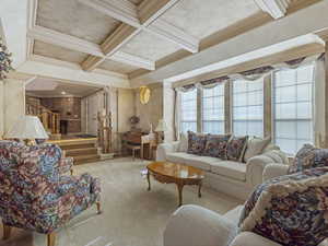 Carpeted living room with coffered ceiling, beamed ceiling, crown molding, stairs, and ornate columns