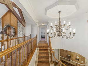 Corridor featuring a tray ceiling, crown molding, and a chandelier