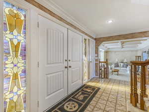 Foyer entrance with coffered ceiling, arched walkways, beam ceiling, and ornamental molding