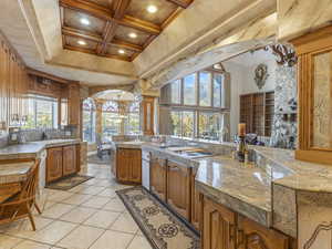 Kitchen with brown cabinetry, tile counters, coffered ceiling, decorative backsplash, and beamed ceiling