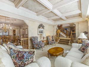 Living room featuring coffered ceiling, beamed ceiling, stairway, arched walkways, and a chandelier