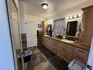 Full bathroom with a textured ceiling, double vanity, and stone tile floors