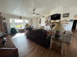 Living room featuring lofted ceiling, wood finished floors, a fireplace, a textured ceiling, and ceiling fan
